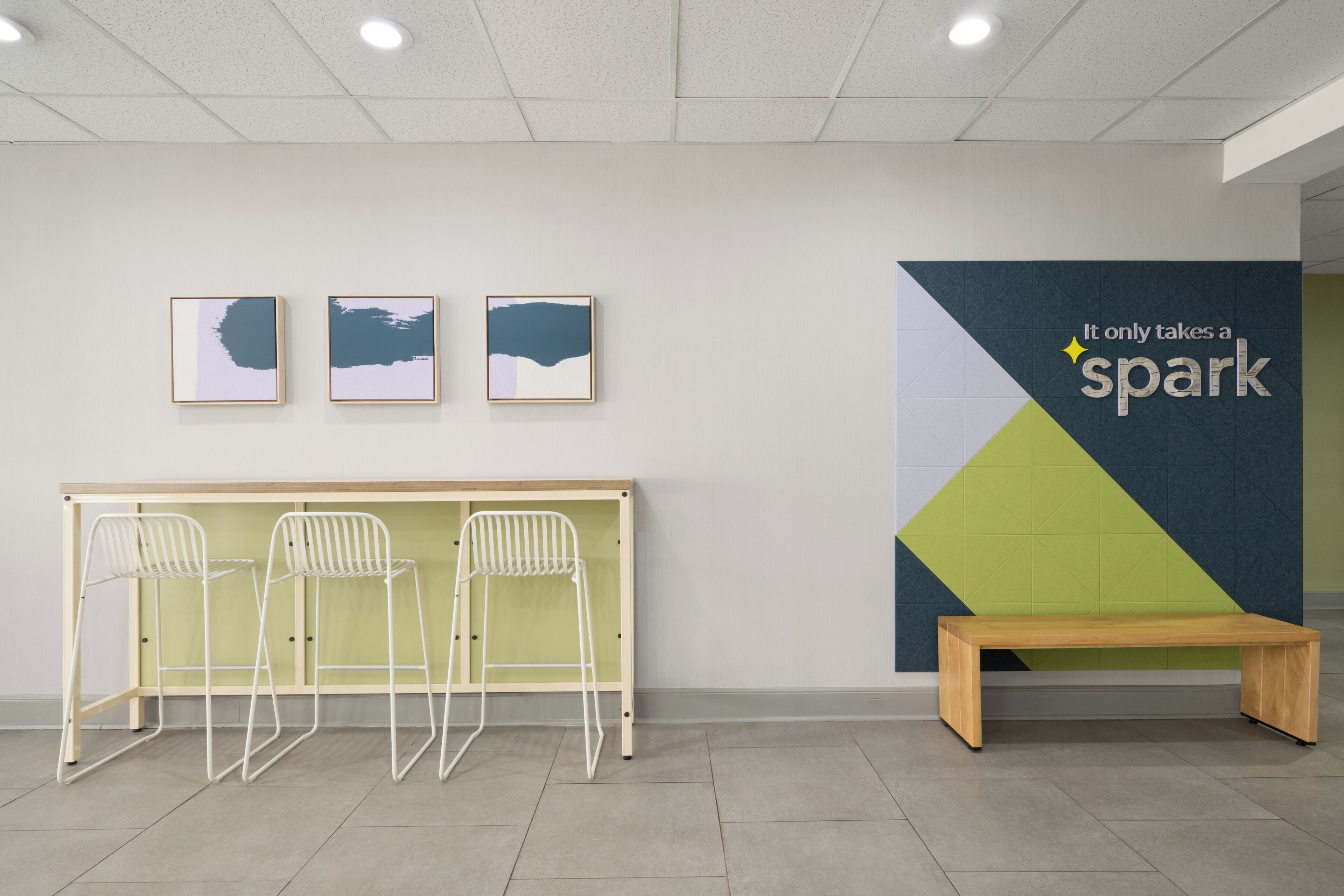 A modern waiting area with a wooden bench, three white metal chairs, and three framed artworks on the wall.