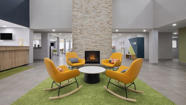 Un vestíbulo moderno con una columna de piedra, una chimenea y sillones mecedores amarillos alrededor de una mesa central.