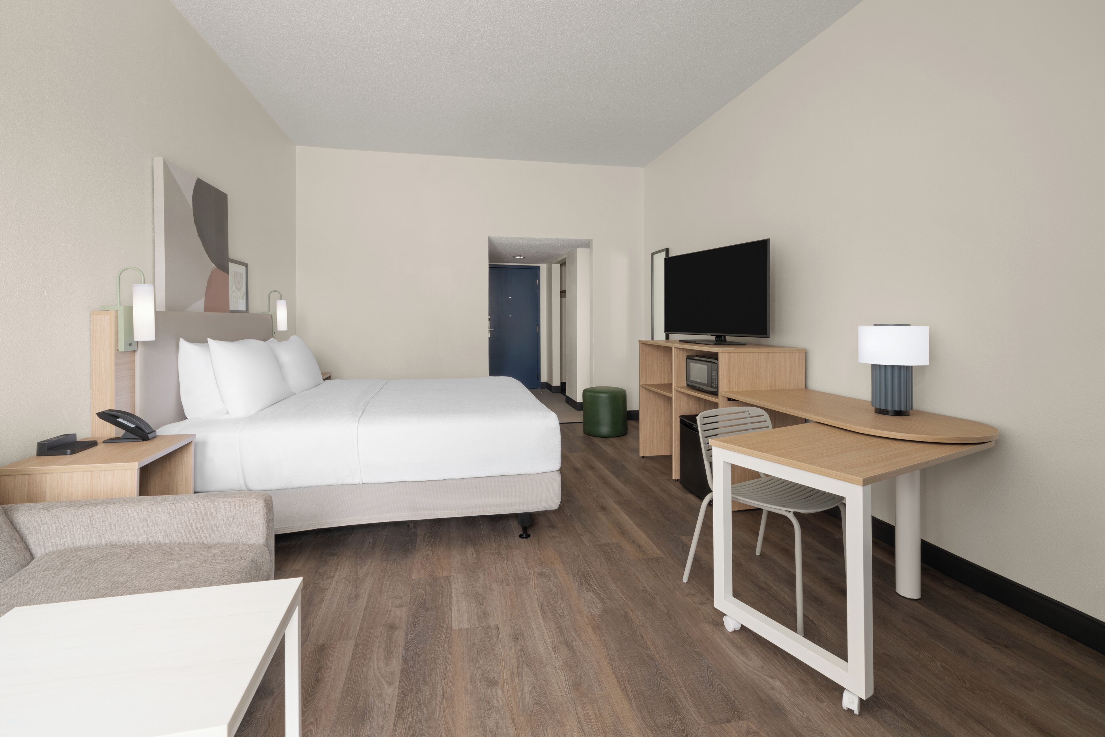 Ett modernt hotellrum med en säng, ett skrivbord, en stol, en tv och en lampa.