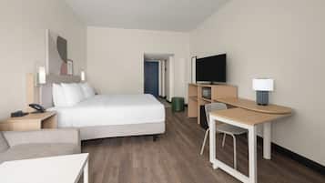 A modern hotel room with a bed, a desk, a chair, a television, and a lamp.