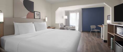 Habitación de hotel con una cama grande, un escritorio, una silla, un televisor y una ventana con cortinas.