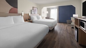 Habitación de hotel con dos camas, un escritorio con silla, un televisor y una ventana con cortinas.