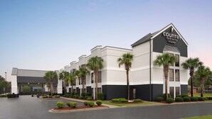 Edificio de Country Inn & Suites by Radisson con estacionamiento y palmeras.