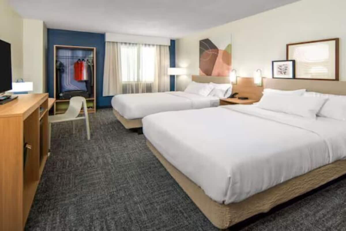 A hotel room with two beds, a desk, a chair, a wardrobe, and a window with curtains.