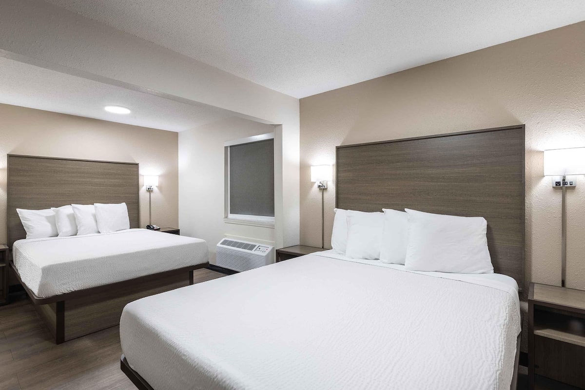 A hotel room with two beds, each with a wooden headboard, white bedding, and bedside lamps.