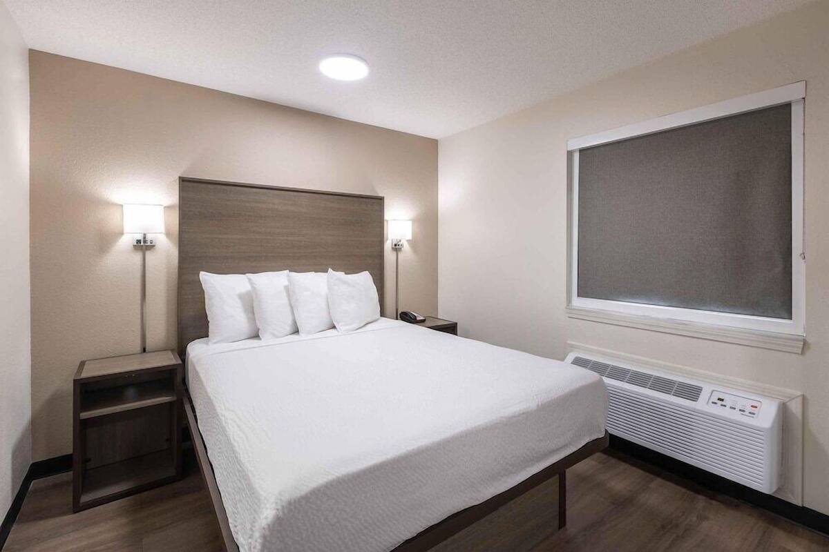 A hotel room with a bed, bedside lamps, a heater, and a window.