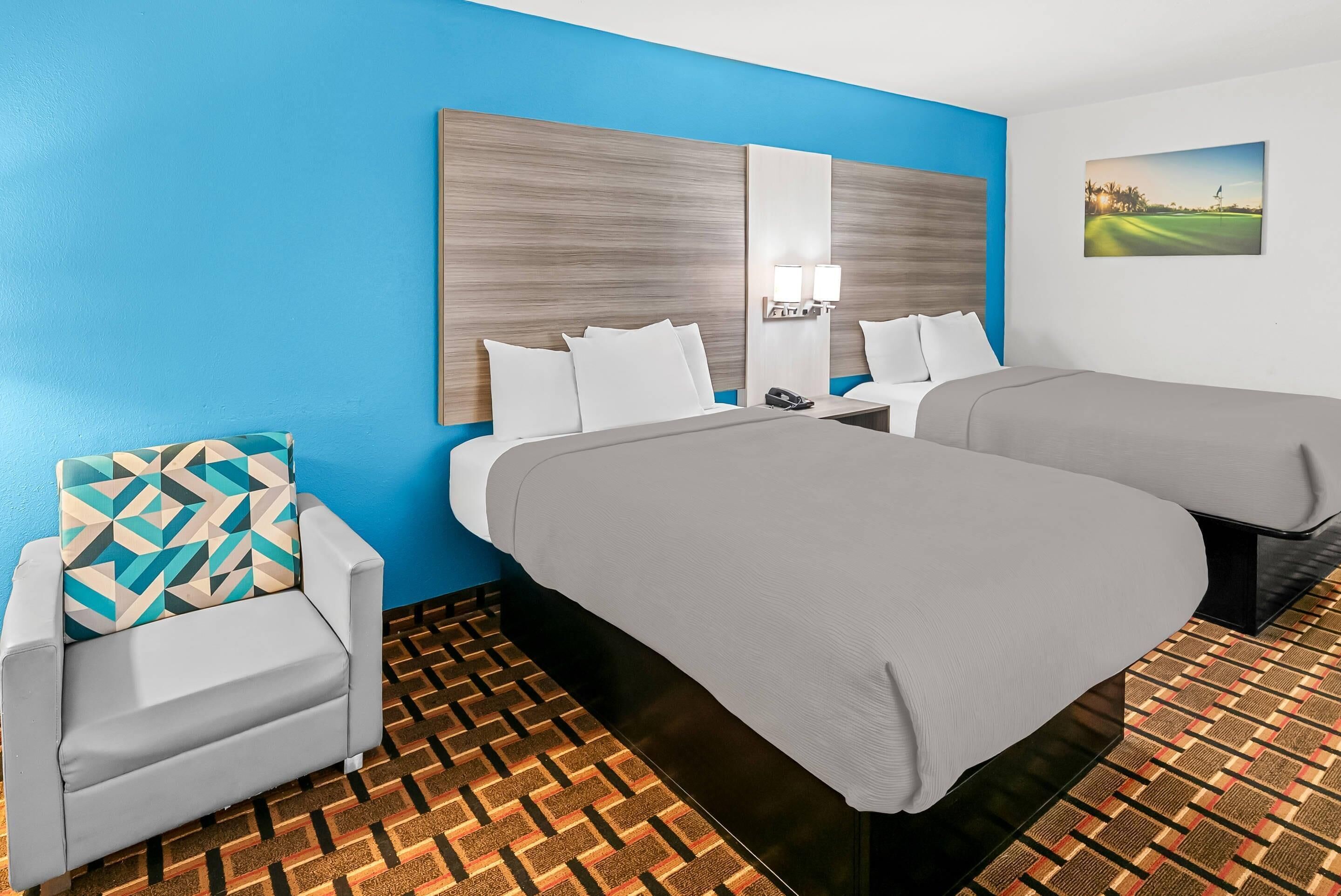 Habitación de hotel con dos camas, un sofá, piso estampado y un cuadro en la pared.