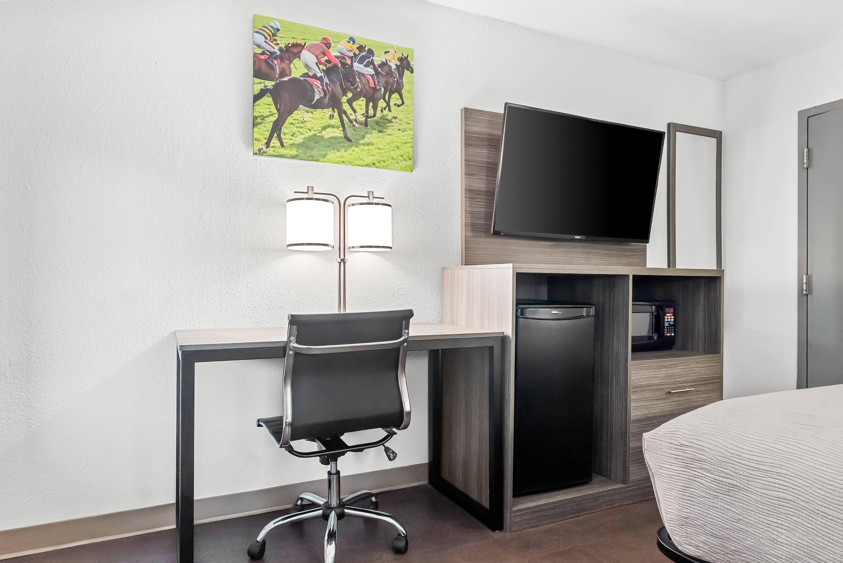 Une chambre d’hôtel équipée d’un bureau, d’une chaise, d’une télévision, d’un four à micro-ondes et d’un lit.