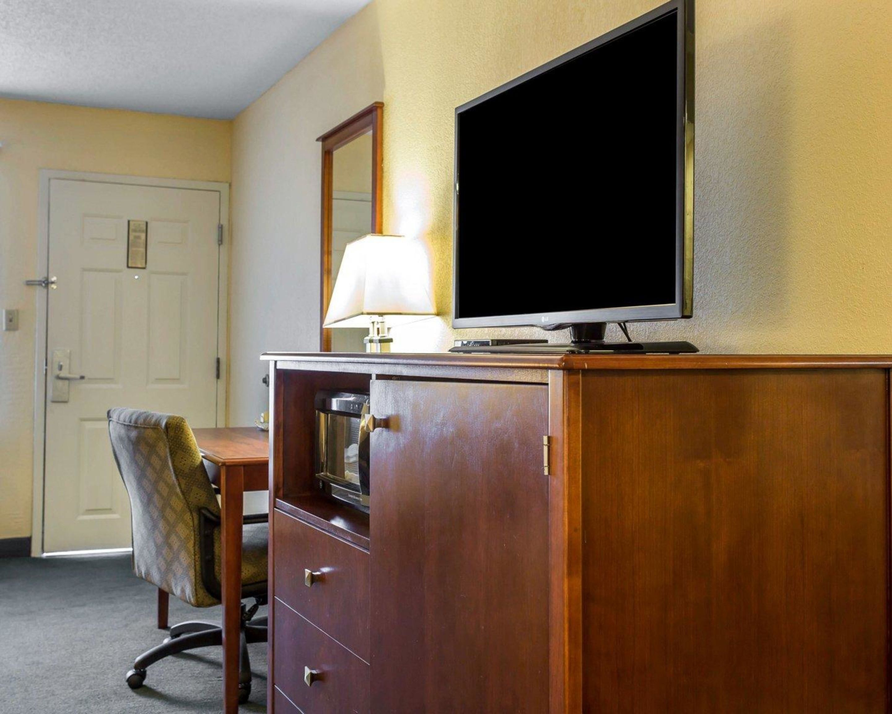 Een hotelkamer met een houten bureau, een televisie erboven, een lamp en een stoel.