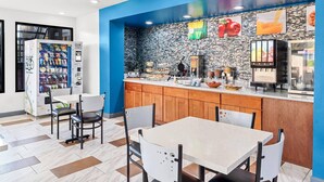 A modern cafe with a blue accent wall, a vending machine, a buffet counter, and a seating area with a herringbone-patterned floor. - Quality Inn Aiken North (Aiken)