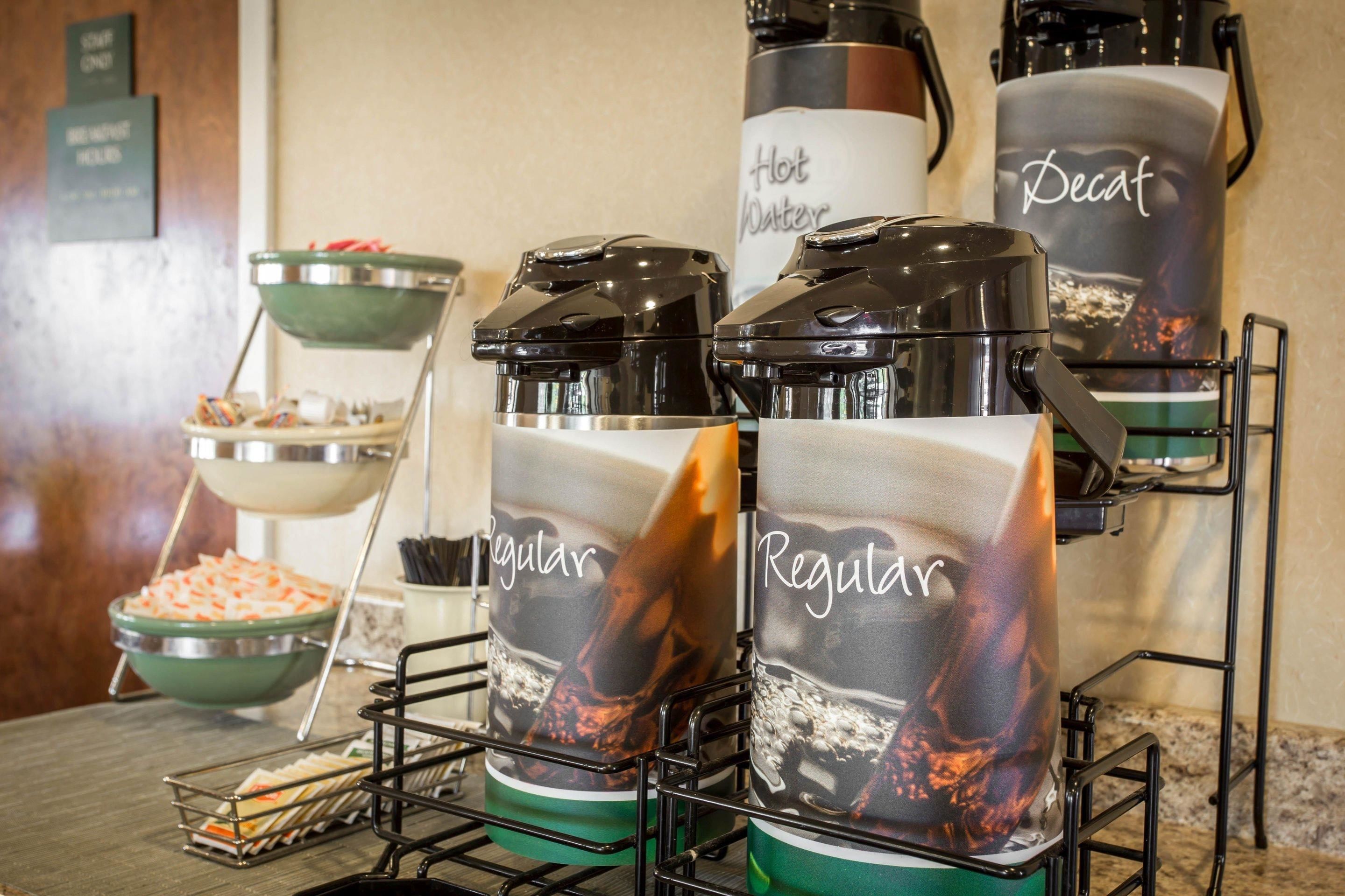 Montaje de bufé con dispensadores de café regular y descafeinado, señalizados como 'Regular' y 'Calentador de agua'.