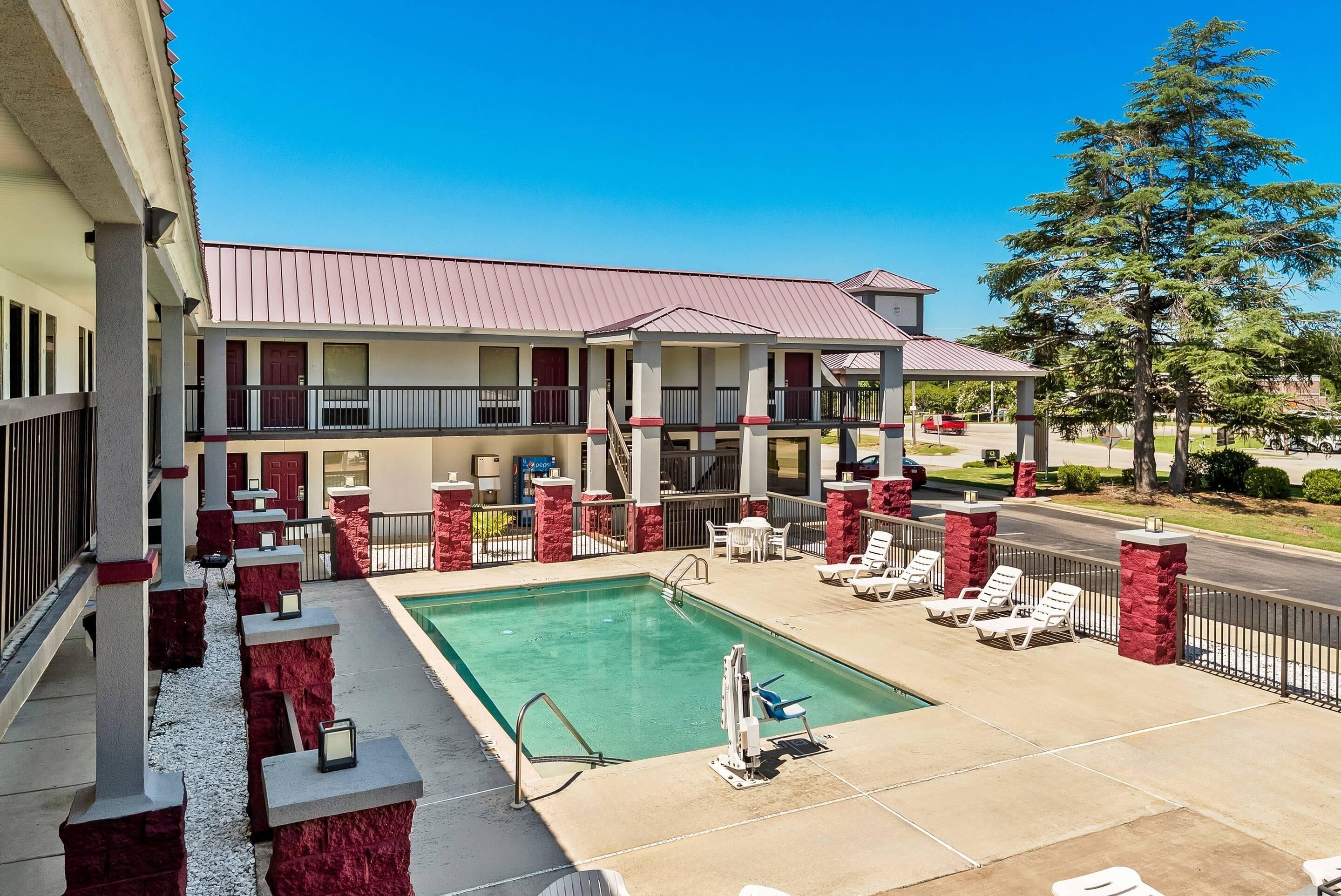 A hotel with a swimming pool, outdoor seating, and a red and white color scheme.