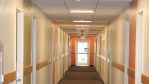 Un long couloir étroit, avec des portes de chaque côté, un sol recouvert de moquette et un éclairage fluorescent.