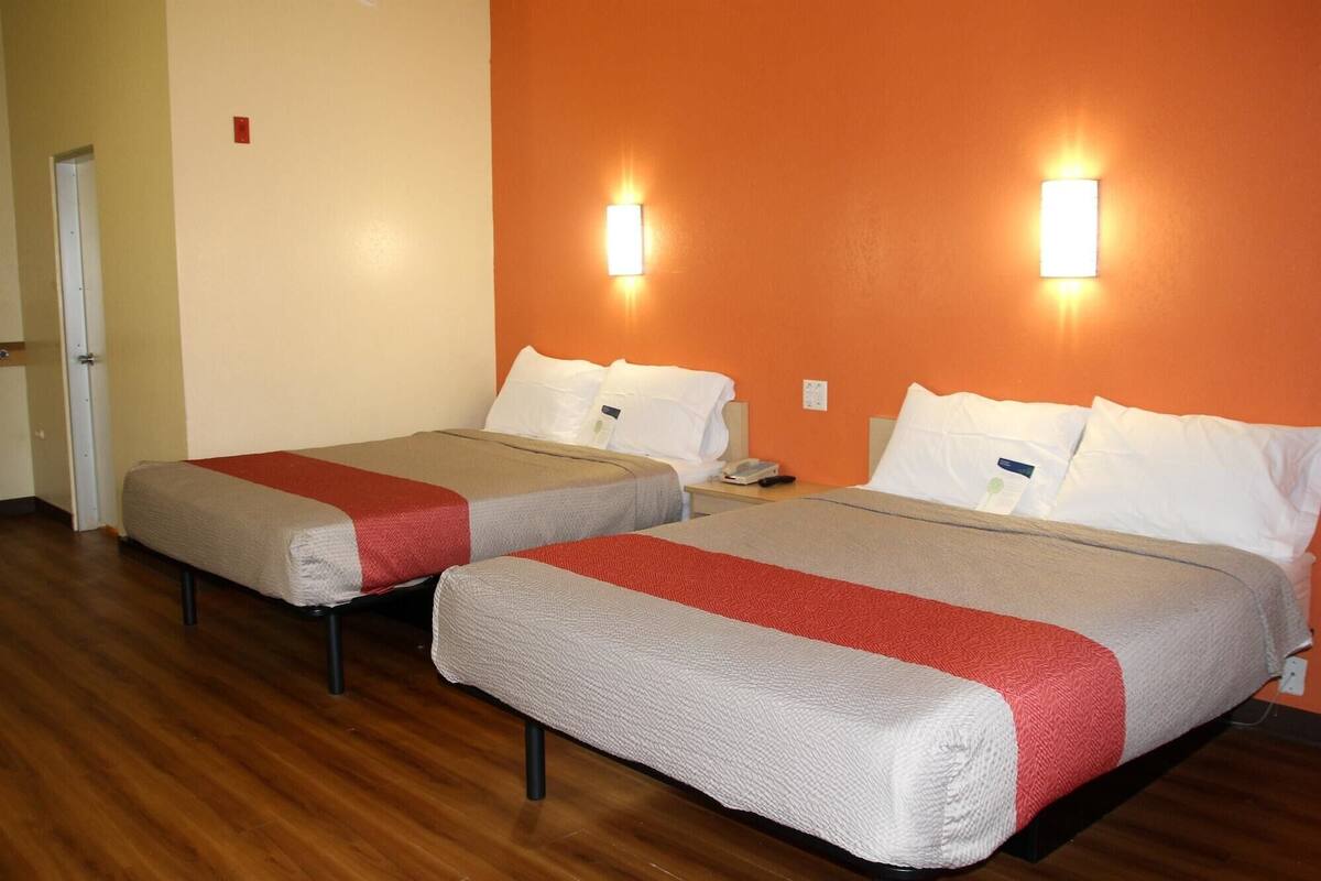 Two beds with red and white bedding, wooden flooring, and wall-mounted lights.