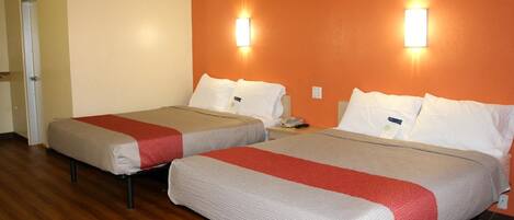 Two beds with red and white bedding, wooden flooring, and wall-mounted lights.
