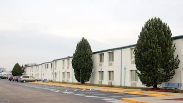 A row of white motel buildings with parking spaces and a few cars parked.