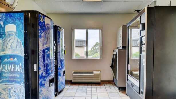Un couloir étroit, avec des distributeurs automatiques d’un côté, une fenêtre donnant sur un bâtiment dont la façade porte l’inscription « SALON » au centre, et un bouton-poussoir sur le mur.
