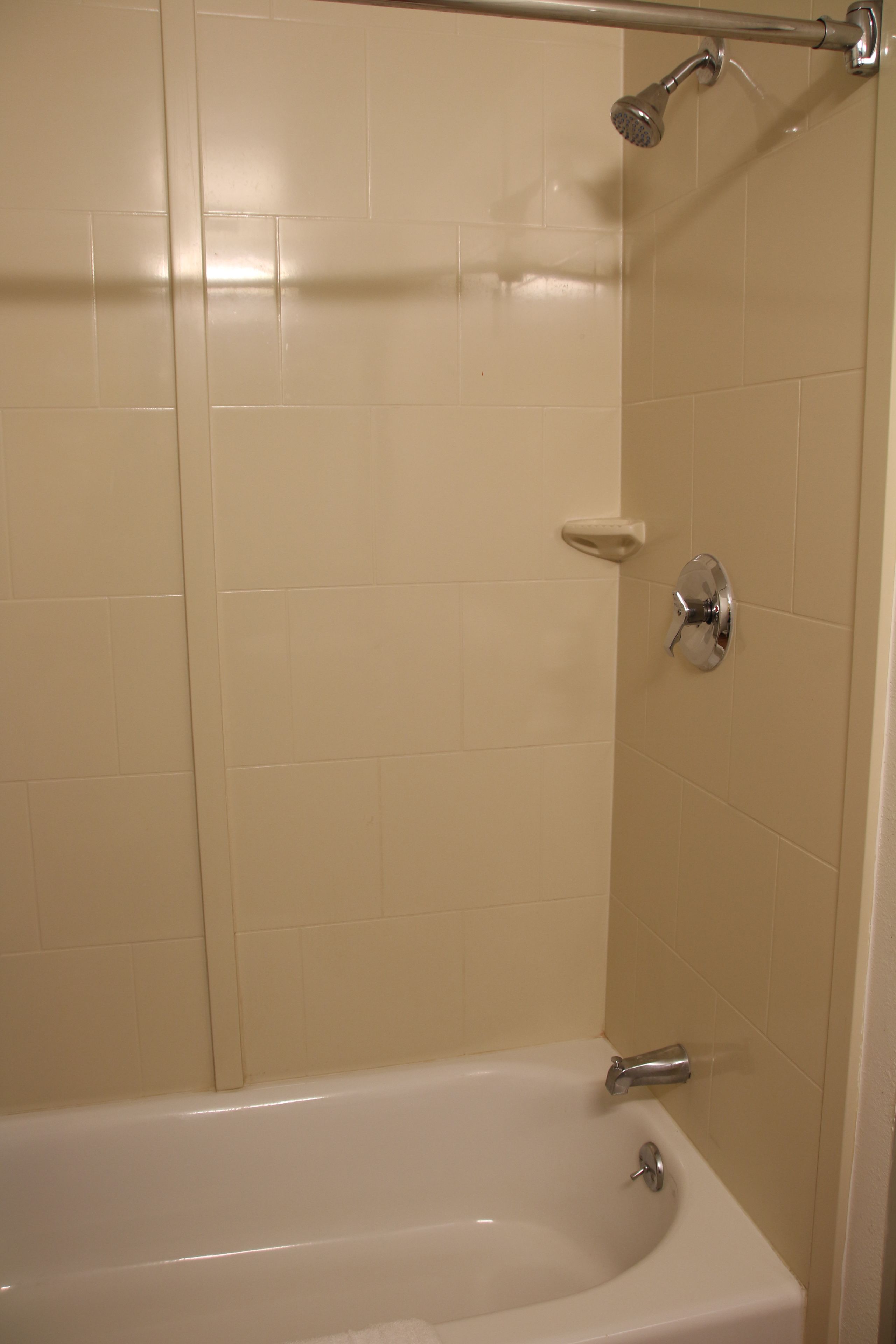 A bathroom with a bathtub, a showerhead, and a hand soap dispenser.