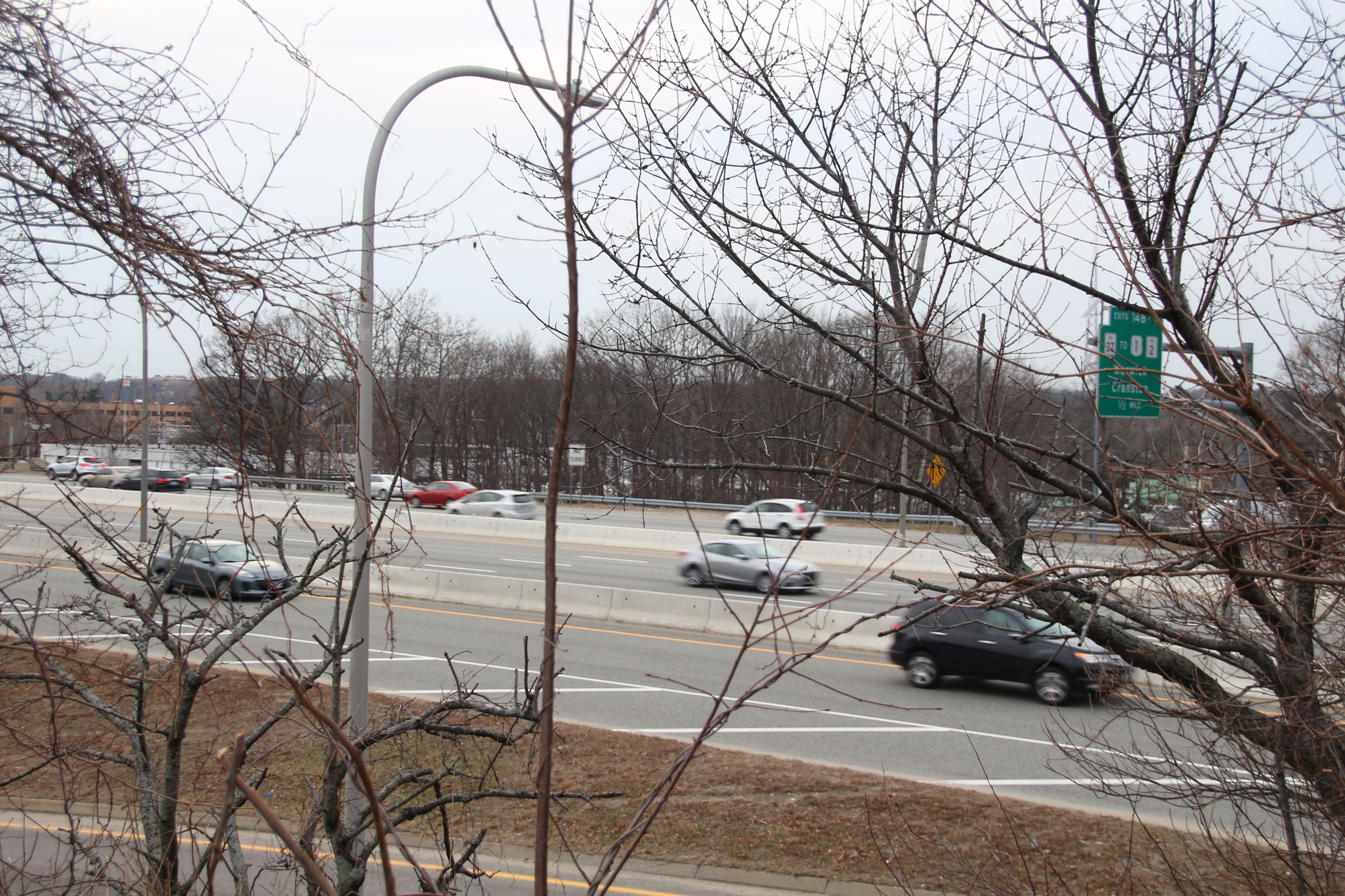A multi-lane highway with cars in motion, surrounded by leafless trees and a street sign.