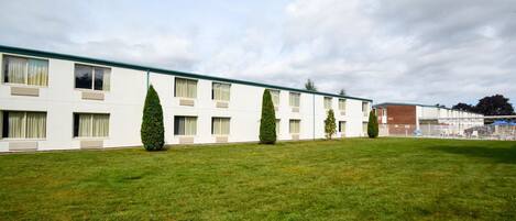 Una hilera de edificios blancos con múltiples ventanas y techo plano, rodeados de un césped cuidado y algunos árboles.