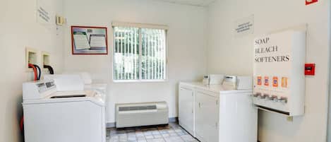 Un cuarto de lavandería con lavadora, secadora y dispensador mural para detergente, lejía y suavizantes.