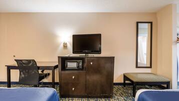 A hotel room with a bed, a desk with a television, a microwave, a chair, and a bench.