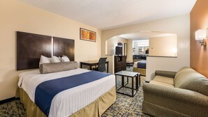 A hotel room with a large bed, a desk, a chair, a sofa, a small table, and a mirror.