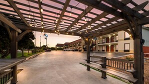 A covered outdoor area with a wooden bench, a building with multiple balconies, and a parking lot. - SureStay Hotel by Best Western Meridian (Meridian)
