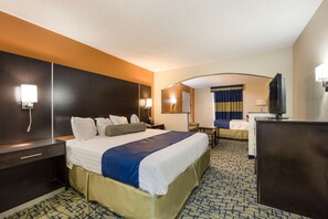 Une chambre d’hôtel avec un grand lit, un bureau, une télévision et une salle de bain visible à travers une arche.