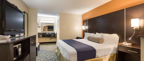 A hotel room with a bed, a TV, a desk with a phone, and a bathroom visible in the background.