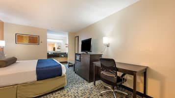 A hotel room with a bed, desk, chair, television, and a small kitchenette.