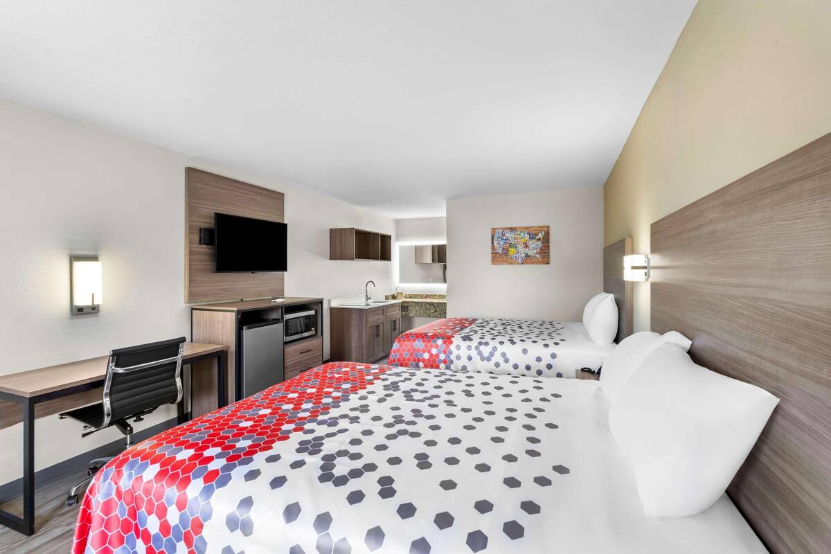 Habitación de hotel con cama, escritorio, silla, televisor, lavamanos y microondas.