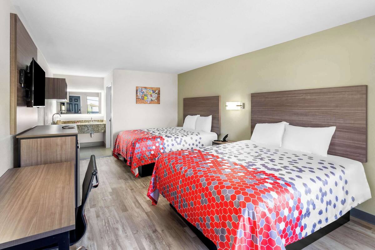 Habitación de hotel con dos camas, un escritorio y una kitchenette.