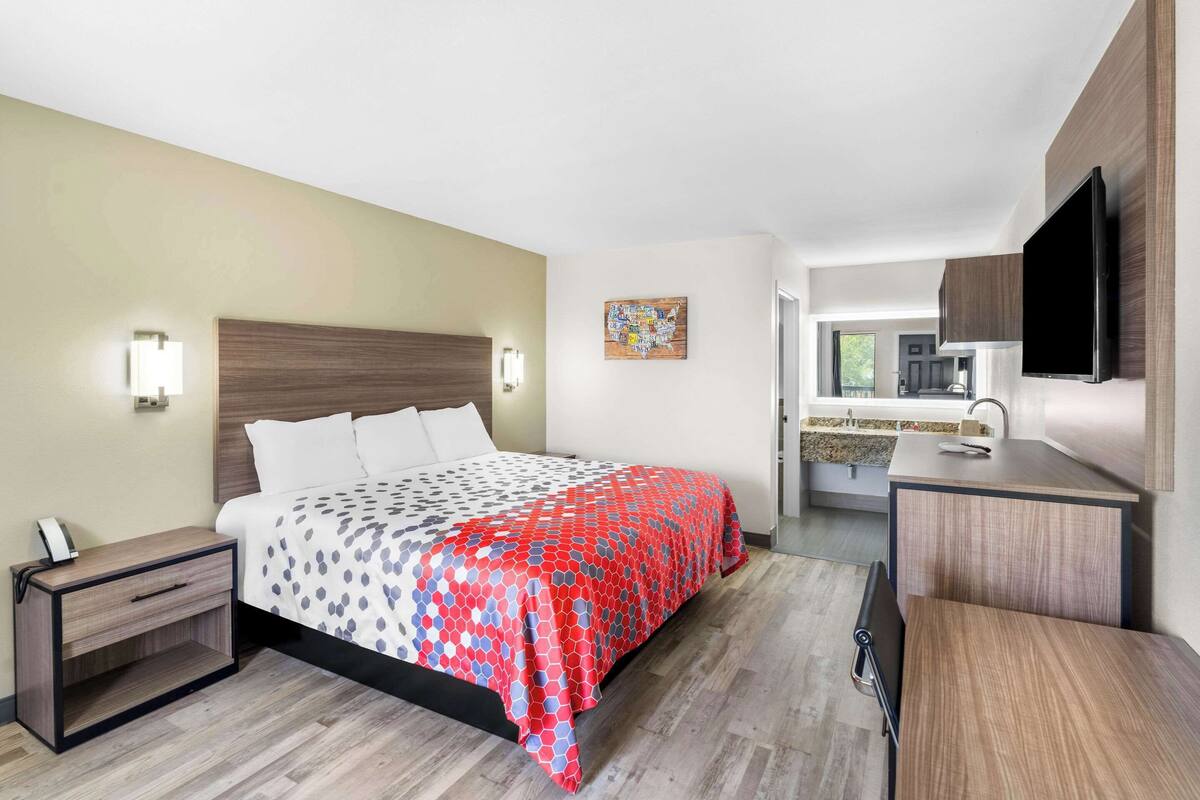 Una habitación de hotel moderna con cama, mesita de noche y vista a la cocina.