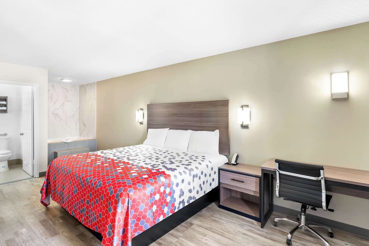 Habitación de hotel con cama, mesita de noche, escritorio, silla y un baño visible a través de una puerta abierta.