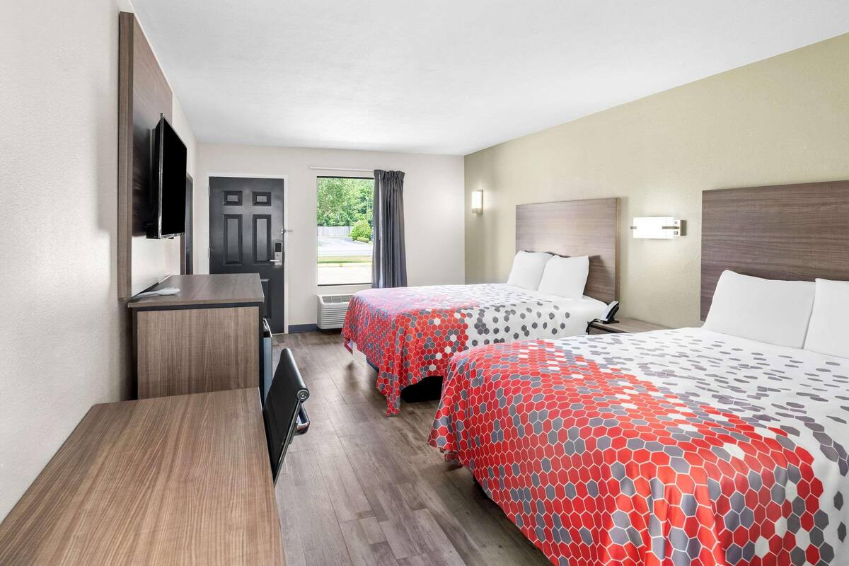 Habitación de hotel con dos camas, un escritorio, un televisor y una puerta que da al exterior.
