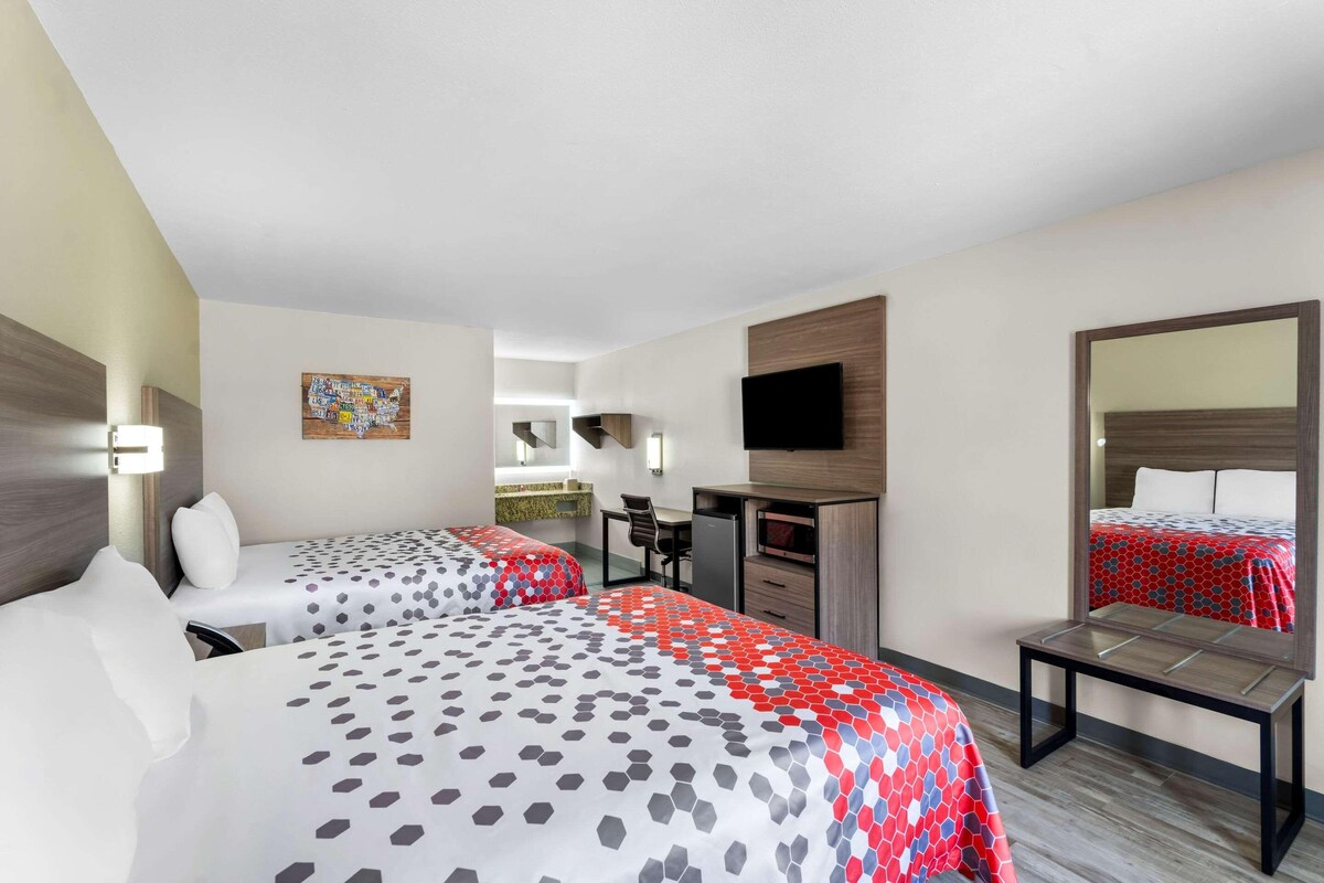 A hotel room with two beds, a desk, a TV, and a mirror.