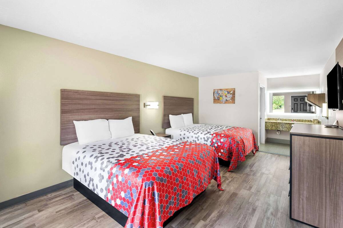 Habitación de hotel con dos camas, un escritorio y vistas al exterior.