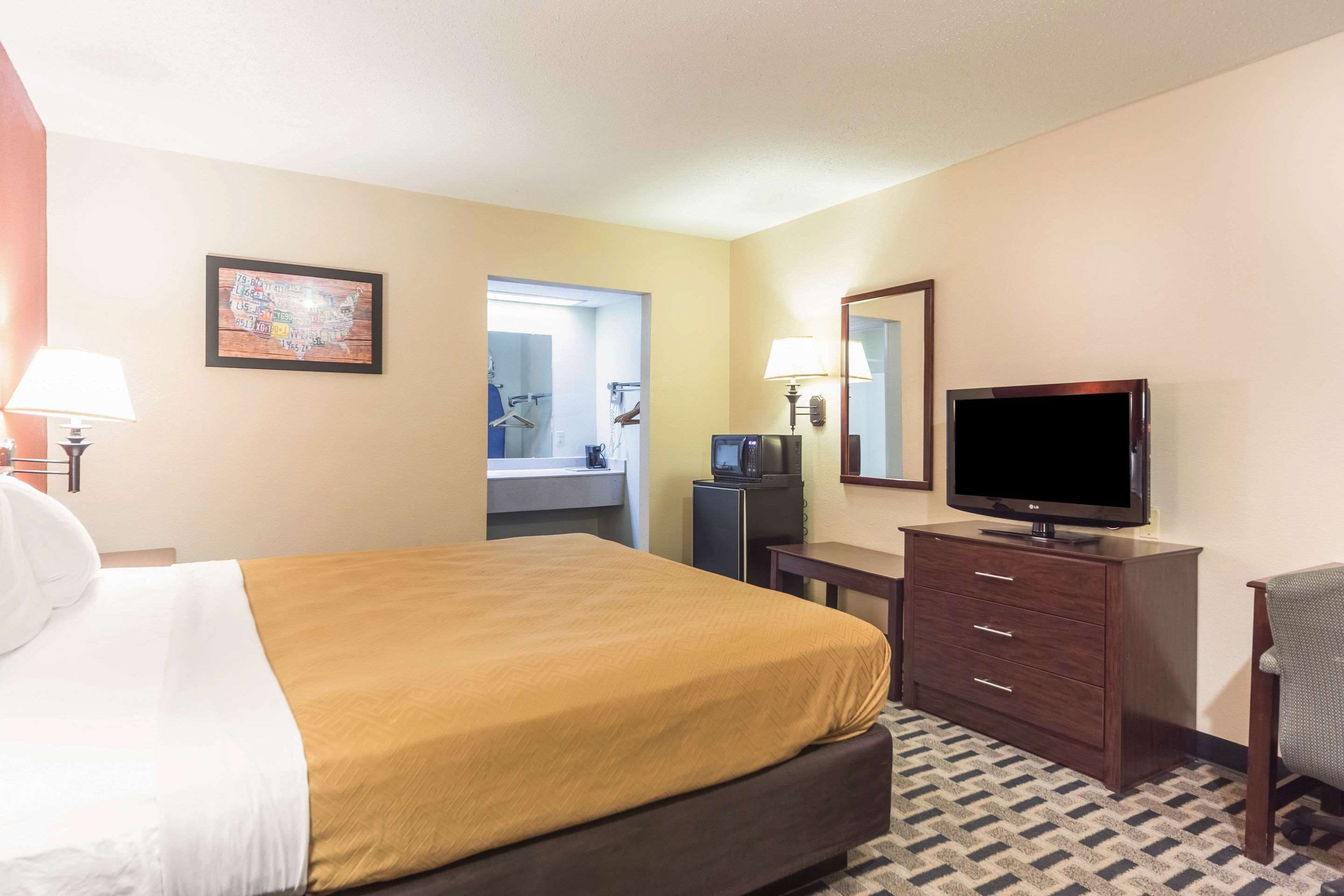A hotel room with a bed, a television, a desk, a chair, a dresser, and a bathroom visible through an open door.