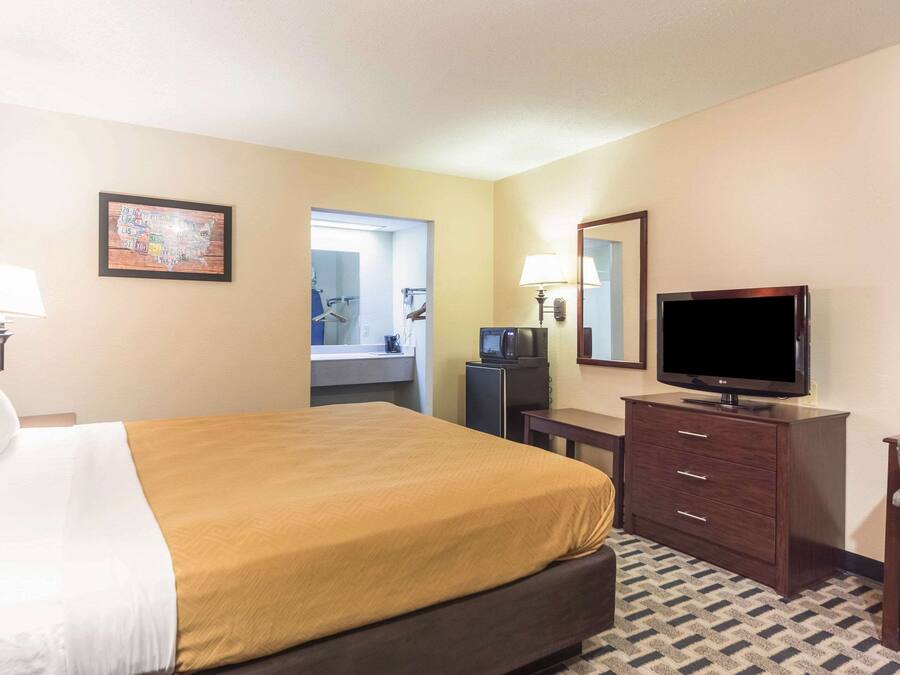 A hotel room with a bed, a television, a desk, a chair, a dresser, and a bathroom visible through an open door.