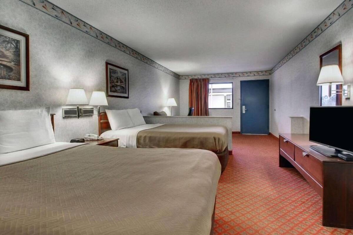 A hotel room with two beds, a television, a desk, and a door.