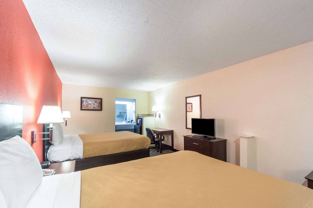 A hotel room with two beds, a desk, a chair, a TV, and a bathroom visible in the background.