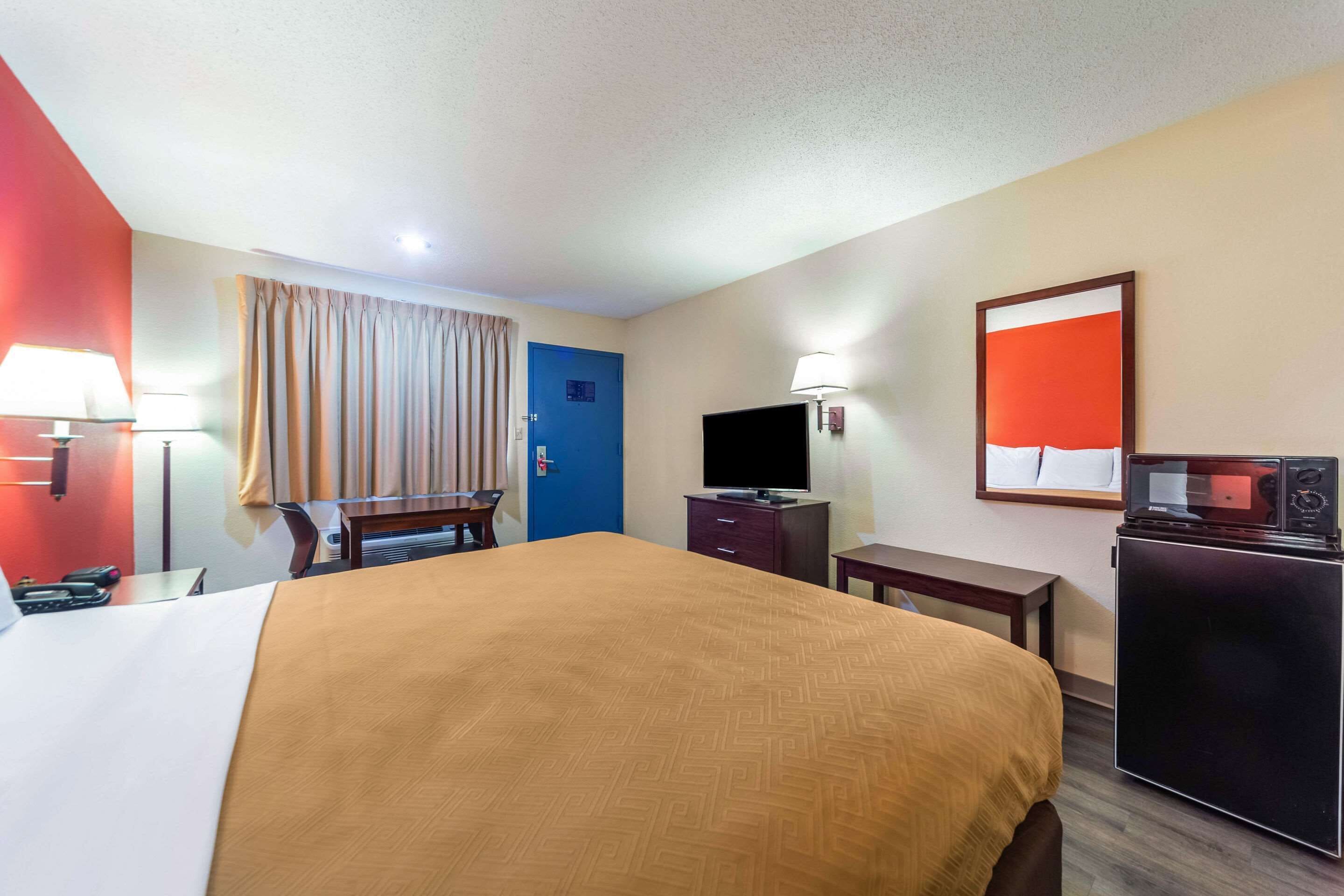 Habitación de hotel con una cama grande, un escritorio, un televisor, un refrigerador y una puerta azul.