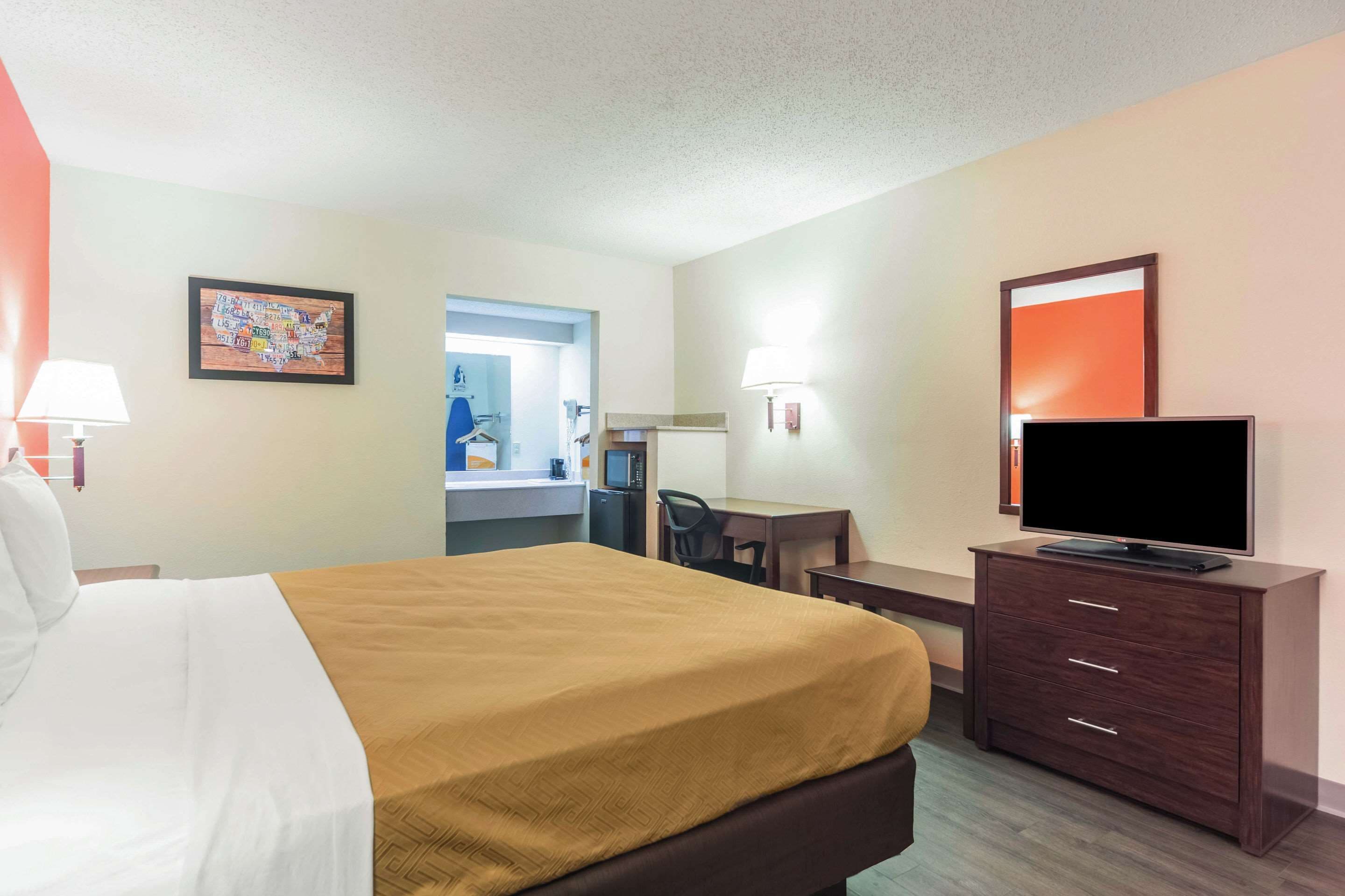 A hotel room with a bed, a desk, a television, and a bathroom visible through an open door.