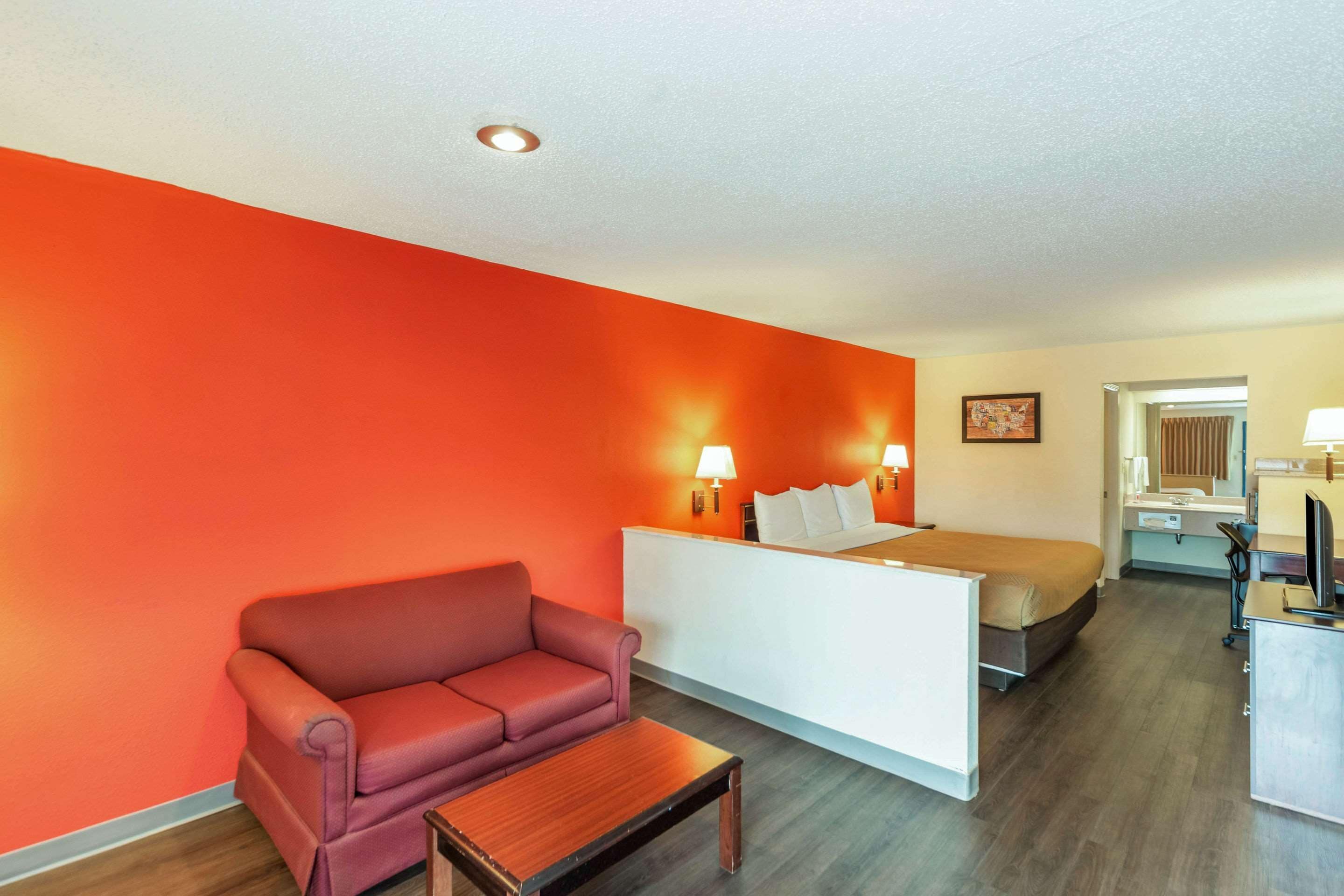 Una habitación de hotel con una pared roja, una cama, un escritorio, una silla y una pequeña mesa.