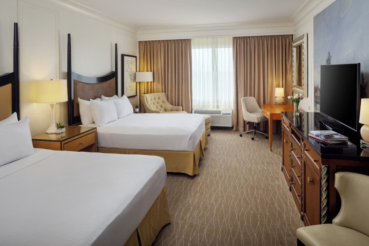 A hotel room with two beds, a desk, a television, and a chair.