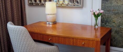 A wooden desk with a lamp and a vase of flowers.
