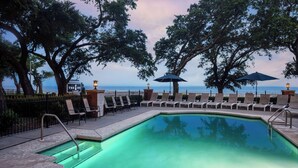 A swimming pool with lounge chairs and umbrellas, surrounded by trees and a view of the ocean. - The Inn at Long Beach (Long Beach)