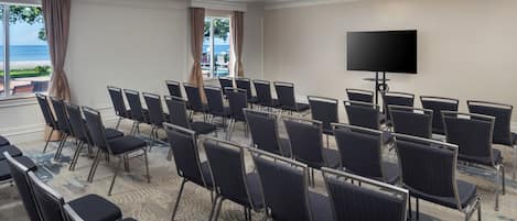 Une salle de conférence avec des rangées de chaises, un grand téléviseur à écran plat et une vue sur la plage par les fenêtres.