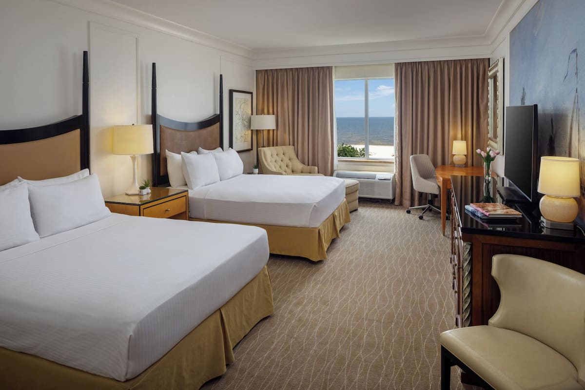 A hotel room with two beds, a desk, a chair, and a television.